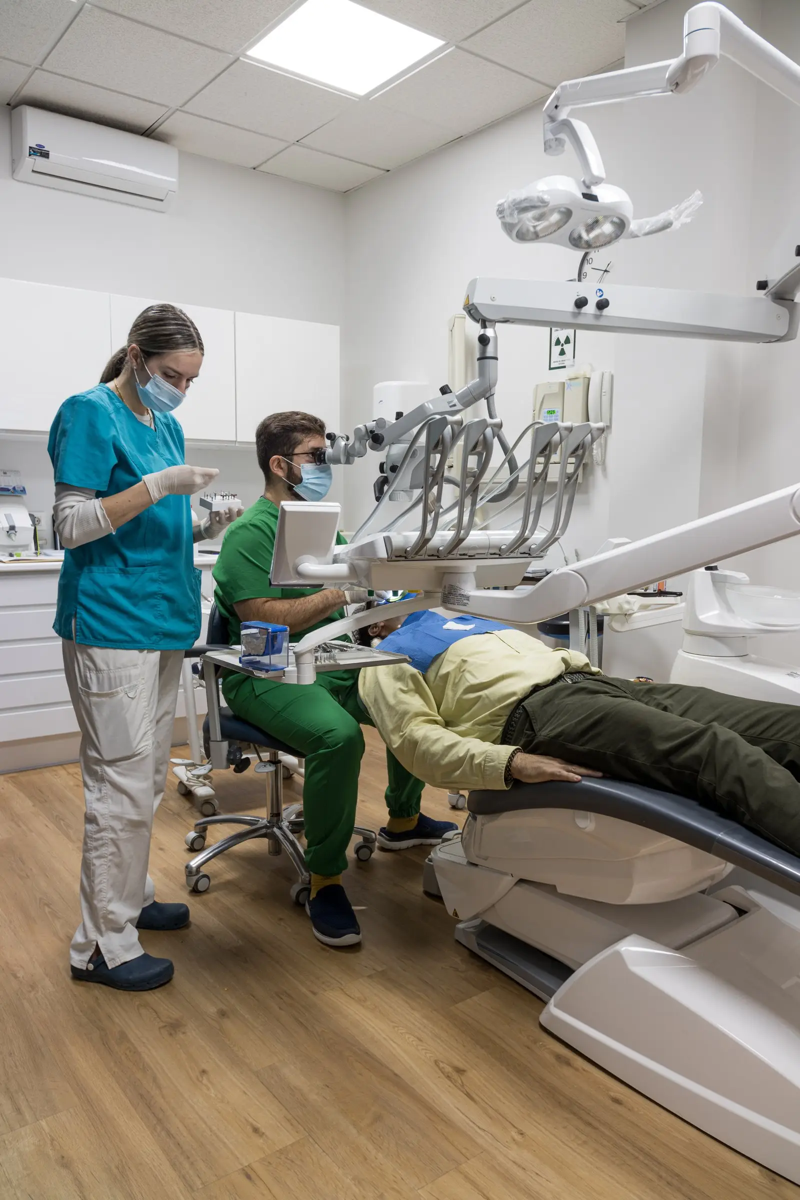 Odontólogo e higienista de Salud Total tratando a un paciente con microscopio